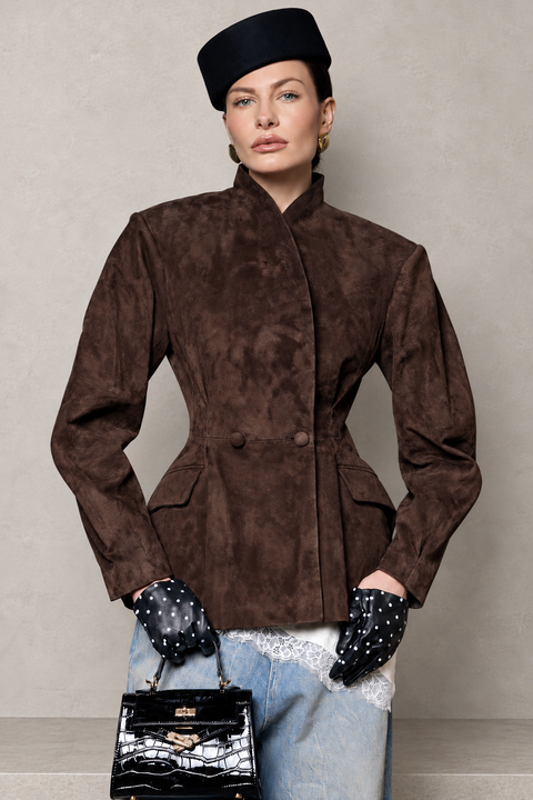 A model wearing a dark brown suede-like double-breasted jacket with a high stand collar, paired with a black beret, black polka-dot gloves, light-wash jeans, and holding a black handbag against a neutral gray background.