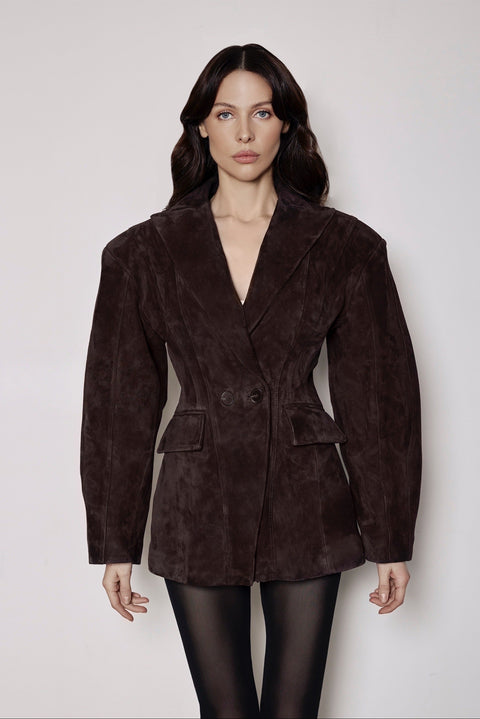 A woman wearing a brown suede blazer tailored with a cinched waist, paired with black tights, blending soft suede with structured elegance for a polished feminine look.