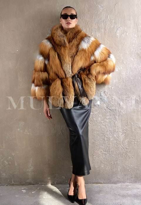 A woman wears a luxurious oversized coat made from genuine red fox fur, cinched at the waist with a sleek leather belt, radiating elegance and warmth in a refined winter look.
