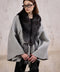 A woman wears a classic cashmere cape trimmed with genuine silver fox fur, effortlessly layering it over her outfit for stylish year-round elegance.