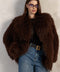 A woman wears a brown Mongolian coat handcrafted from the thickest, softest genuine Mongolian fur, featuring a dramatic collar, long sleeves, and elegant snap and hook closures.