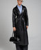 A woman wears a bold black leather coat with wide, structured shoulders, paired with wide trousers and a sleek black fashion leather bag, exuding modern power dressing.